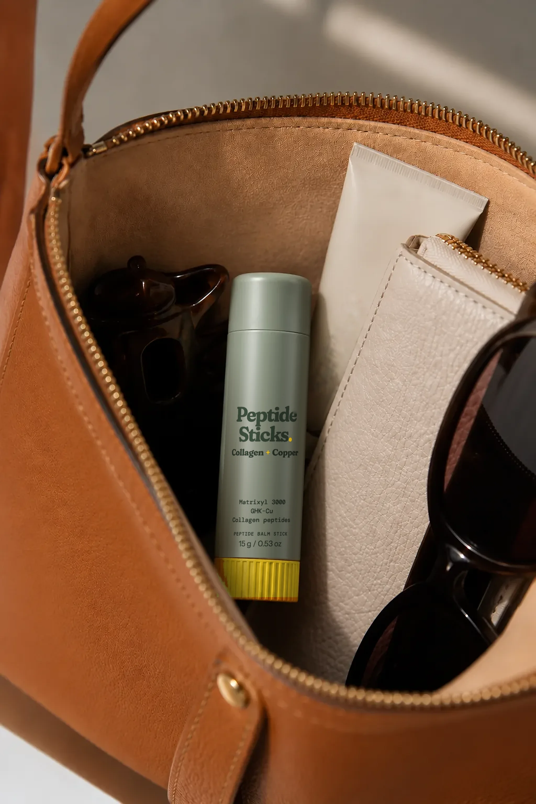 Collagen + Copper Stick in an open leather bag beside everyday essentials