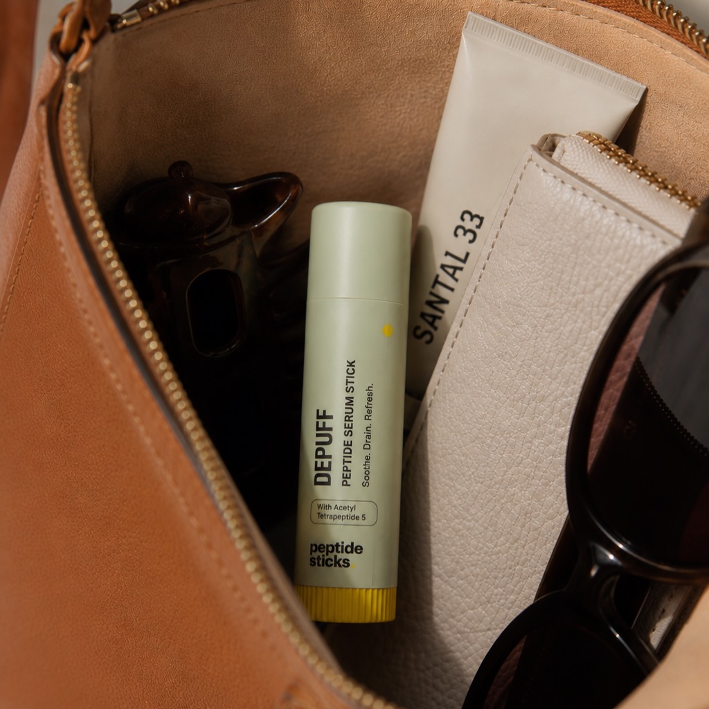 Depuff Peptide Eye Stick packed in a handbag with sunglasses and daily essentials