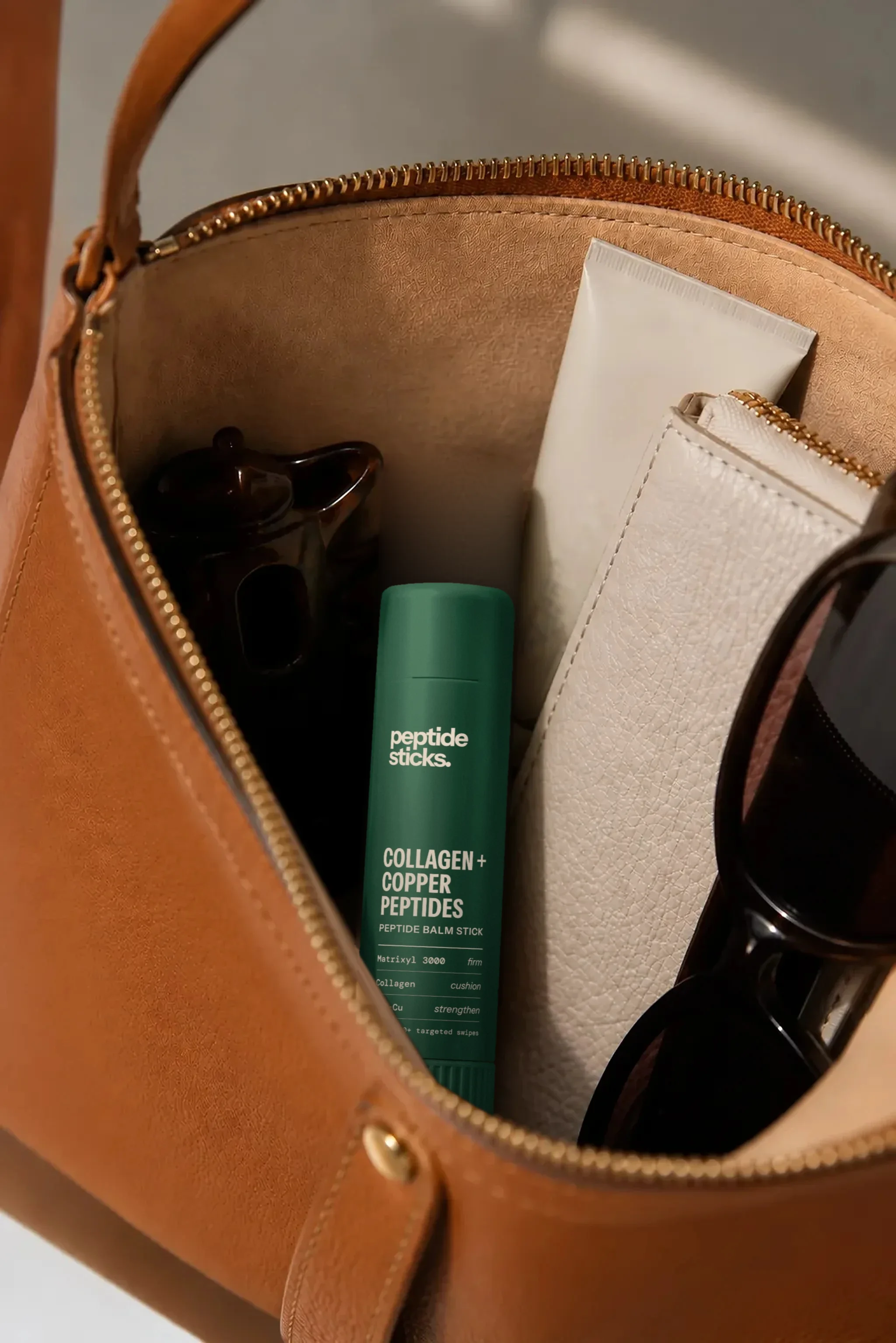 Collagen + Copper Stick in an open leather bag beside everyday essentials