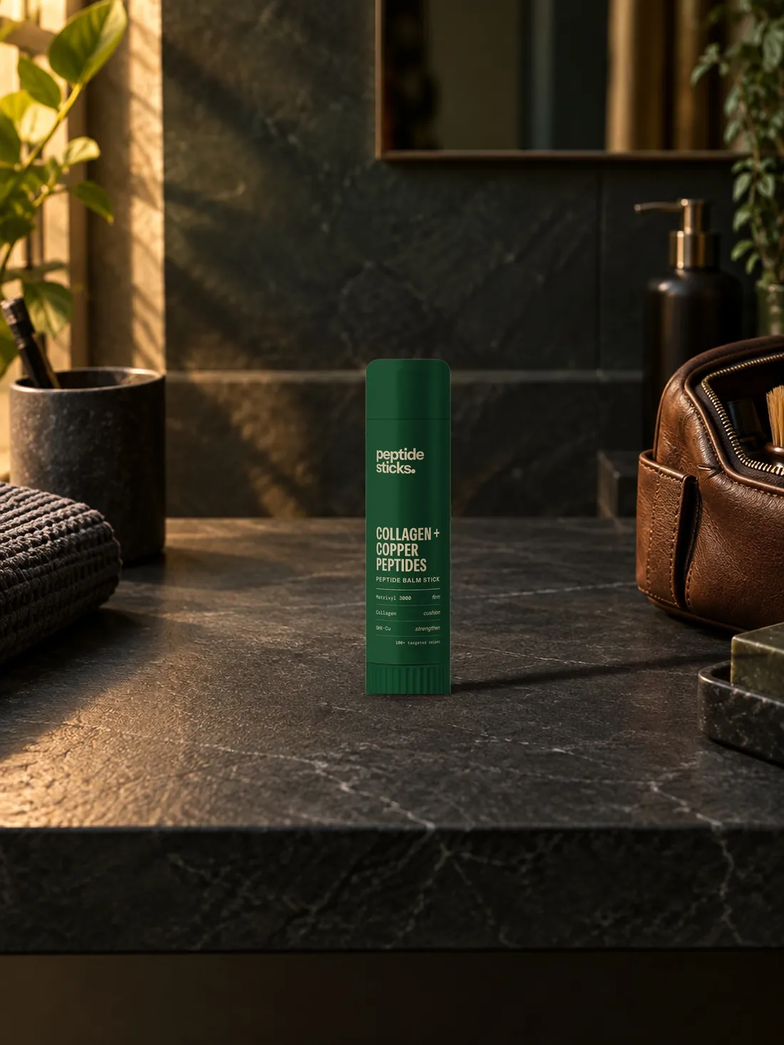 The Collagen + Copper Stick on a dark slate counter beside a leather wash bag